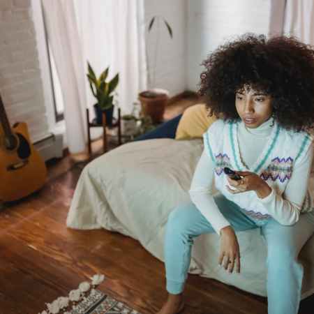 calm young ethnic woman watching tv sitting on couch during weekend at home